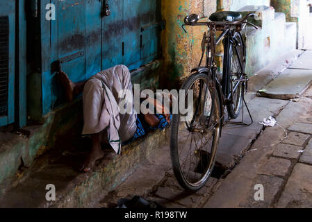 Kumbakonam, India - 21 agosto 2018: il vecchio uomo è in appoggio giacente nella parte anteriore di un negozio chiuso nel mercato Kumbakonan Foto Stock