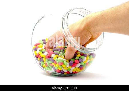 La mano in un barattolo con caramelle colorate su sfondo bianco Foto Stock