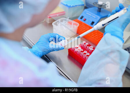 Test del DNA in laboratorio. Un tecnico di laboratorio con un erogatore nelle sue mani sta conducendo le analisi del DNA in un laboratorio sterile dietro il vetro. Foto Stock