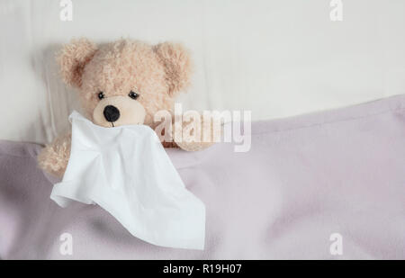 Freddo, canna fumaria o allergia concetto. Grazioso orsacchiotto a letto, coperto con una calda coperta, tenendo un tessuto Foto Stock