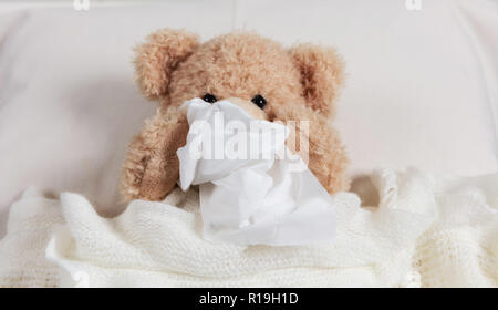 Freddo, canna fumaria o allergia concetto. Grazioso orsacchiotto a letto, coperto con una calda coperta, tenendo un tessuto Foto Stock