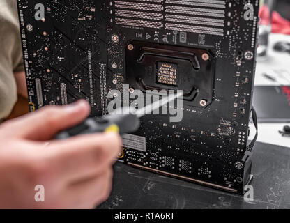 Lo specialista installa un raffreddatore sul nuovo processore contro lo sfondo di un computer scheda madre Asus rog crosshair vii eroe. Foto Stock