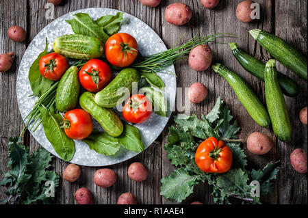 Produrre una scena di raccolti di fresco cetriolo, pomodori, patate rosse, kale, zucchini e kale su un sfondo rustico. Foto Stock