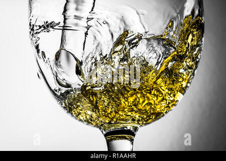 Flusso di vino bianco versando in un bicchiere di vino bianco, splash close-up su sfondo grigio. Foto in bianco e nero con il colore del vino. Foto Stock