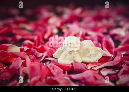 Statuetta di due antichi poco adorabile angeli di gesso sulla pietra nera con sfondo rosa peonia petali di fiori. Amore vintage, romantico, Valen Foto Stock