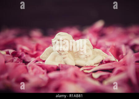 Statuetta di due antichi poco adorabile angeli di gesso sulla pietra nera con sfondo rosa peonia petali di fiori. Amore vintage, romantico, Valen Foto Stock