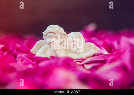 Statuetta di due antichi poco adorabile angeli di gesso sulla pietra nera con uno sfondo viola rosa peonia petali di fiori. Amore, romantico, Valent Foto Stock