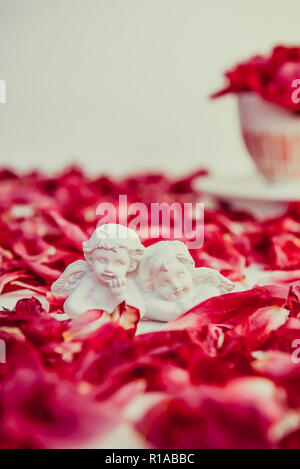 Statuetta di due antichi piccoli angeli incantevole del gesso su sfondo bianco con rosa peonia viola petali di fiori. Amore, romantico, Valentines d Foto Stock