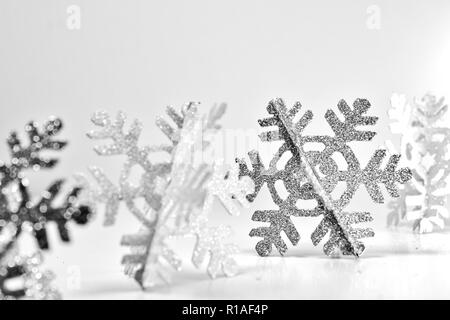 Glittery fiocchi di neve in una riga con un fiocco di neve in argento nel fuoco su sfondo bianco. Luminosa scena invernale Foto Stock