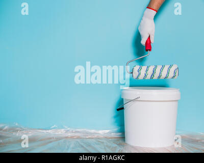 Immagine della vernice può e uomo di contenimento del rullo di vernice nella parte anteriore della parete di blu. Foto Stock