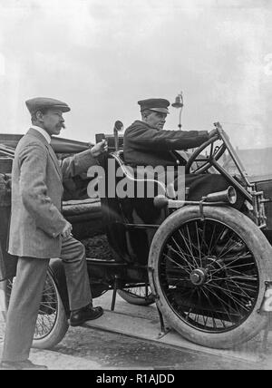 Una fotografia in bianco e nero scattate durante l'inizio del XX secolo che mostra due uomini e un vintage automobile. Un uomo dietro il volante e un uomo in piedi con un piede sulla pedana della vettura. Foto Stock