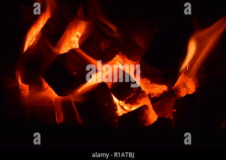 Close up di mattonelle di lignite sul fuoco con rosso giallo dentro le fiamme di un solido speciale forno, rosso e arancione texture sfocate su uno sfondo nero. Foto Stock