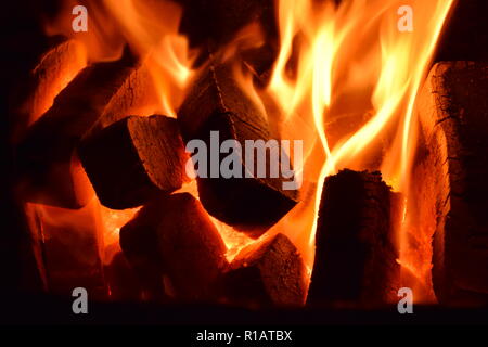 Close up di mattonelle di lignite sul fuoco con rosso giallo dentro le fiamme di un solido speciale forno, rosso e arancione texture sfocate su uno sfondo nero. Foto Stock