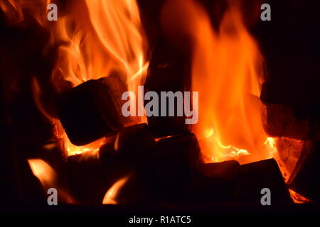 Close up di mattonelle di lignite sul fuoco con rosso giallo dentro le fiamme di un solido speciale forno, rosso e arancione texture sfocate su uno sfondo nero. Foto Stock