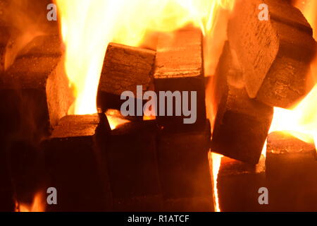 Close up di mattonelle di lignite sul fuoco con rosso giallo dentro le fiamme di un solido speciale forno, rosso e arancione texture sfocate su uno sfondo nero. Foto Stock