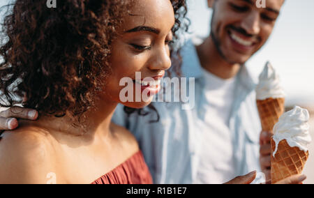 Sorridente giovane mangiare cono gelato in piedi all'esterno. Coppia romantica godendo di gelato. Foto Stock
