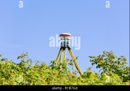 Il GNSS-ricevitore geodetico montato su un treppiede vecchio contro lo sfondo del cielo blu e foglie di lamponi selvatici cespugli. Applicazione pratica nel Foto Stock