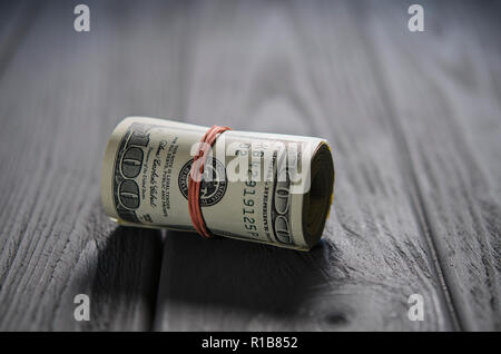 Una spessa rotolo di centinaia di dollari di banconote legate a rosso la banda di gomma si trova sul grigio tavolo in legno Foto Stock