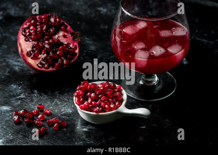 La tentazione di melograno rosso, semi e succo di frutta fresco con l'aggiunta di ghiaccio su un nero, sfondo di pietra Foto Stock