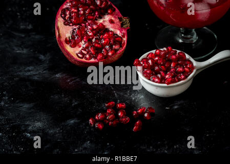 La tentazione di melograno rosso, semi e succo di frutta fresco con l'aggiunta di ghiaccio su un nero, sfondo di pietra Foto Stock
