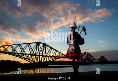 Piper Louise Marshall, indossando una speciale commemorativa tartan rosso, riproduce della battaglia O'er, la musica tradizionale scozzese lamento svolto alla fine della battaglia, all'alba a fianco del Ponte di Forth a North Queensferry sul centesimo anniversario della firma dell'armistizio che ha segnato la fine della Prima Guerra Mondiale. Foto Stock