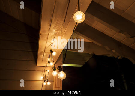 Decorative luci strada appeso sulla terrazza di una casa in legno di notte. Vecchie lampade decorative, illuminazione di festa Foto Stock