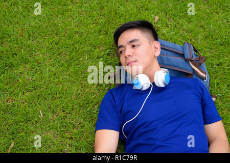 Bel giovane uomo asiatico di relax presso il parco con le cuffie Foto Stock