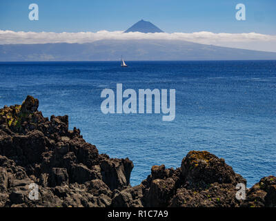 Immagine da una scogliera con una barca a vela in Atlantico e dell'isola di Pico con Pico Mountain in background Azzorre Portogallo Europa Foto Stock