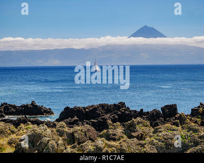 Immagine da una scogliera con una barca a vela in Atlantico e dell'isola di Pico con Pico Mountain in background Azzorre Portogallo Europa Foto Stock