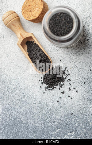 Nero semi di cumino su un cucchiaio di legno e in un vaso di vetro su uno sfondo grigio. Messa a fuoco selettiva Foto Stock
