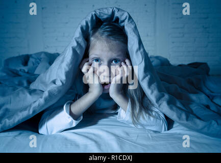 Carino addormentato ragazza urlando e piangendo dopo aver paura o ricalcatura sogno copertura lei stessa con coperta in letto a notte in mood illuminazione drammatica in Foto Stock