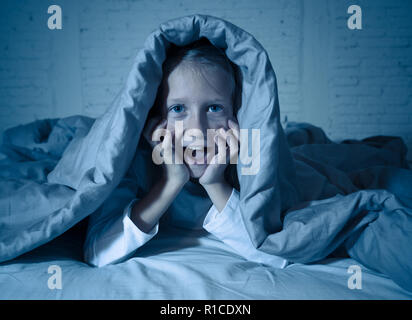 Carino addormentato ragazza urlando e piangendo dopo aver paura o ricalcatura sogno copertura lei stessa con coperta in letto a notte in mood illuminazione drammatica in Foto Stock