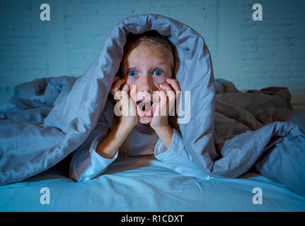 Carino addormentato ragazza urlando e piangendo dopo aver paura o ricalcatura sogno copertura lei stessa con coperta in letto a notte in mood illuminazione drammatica in Foto Stock