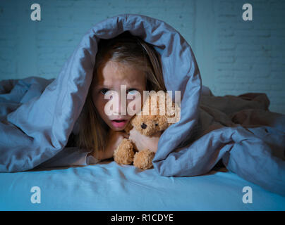 Carino addormentato ragazza urlando e piangendo dopo aver paura o ricalcatura sogno copertura lei stessa con coperta in letto a notte in mood illuminazione drammatica in Foto Stock