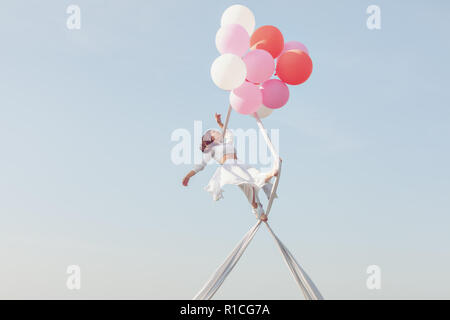 Giovane donna facendo acrobazie in aria su tele bianche. Foto Stock