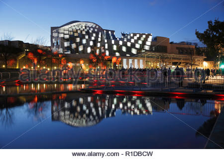 Edinburgh, Regno Unito. 11 Novembre, 2018. L'edificio del parlamento scozzese illuminata sul il giorno dell'Armistizio con immagini che raccontano la storia della guerra mondiale 1 conflitto a fianco di un rotolo di onore di coloro che sono morti, riflesso nel laghetto ornamentale. Credito: Craig Brown/Alamy Live News. Foto Stock