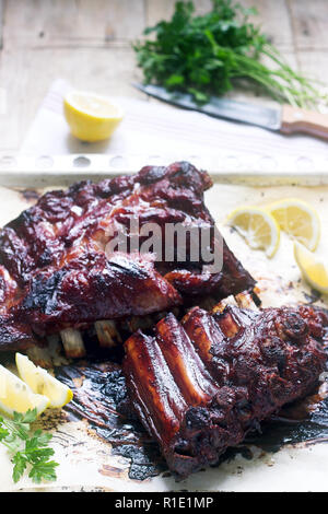 Stuzzicanti cotto smaltato o di vitello costolette di maiale servito con limone e erbe aromatiche. Messa a fuoco selettiva. Foto Stock