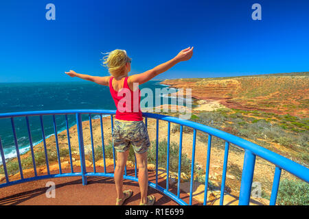 Felice donna backpacker ad Eagle Gorge piattaforma di avvistamento di Kalbarri National Park, Australia occidentale. Ragazza caucasica godendo di scogliere della costa dell'Oceano Indiano. Outback australiano. Cielo blu d'estate. Foto Stock