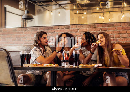 Crazy giovani amici di alimentare ciascun altro trancio di pizza al ristorante. I giovani allegri godendo di mangiare in un fast food cafe. Foto Stock