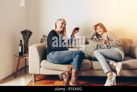 Due felici donne gustando un bicchiere di vino seduti su un lettino a casa. Foto Stock