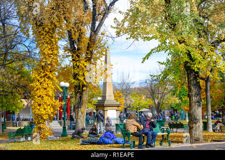 Durante il fogliame di autunno cambia, e il peperoncino rosso ristras appeso dalla lampada posy, persone passeggiare e godersi la Plaza nel centro della città di Santa Fe, NM Foto Stock