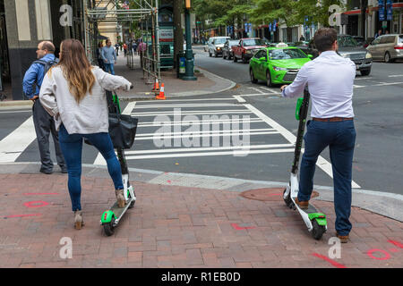 CHARLOTTE, NC, Stati Uniti d'America-11/08/18: un uomo e una donna su scooter elettrici, in attesa di attraversare una strada. Foto Stock