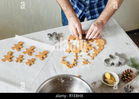 Gastronomia natalizia concetto. L'uomo la cottura gingerbread man cookies nel Natale tavolo in legno nella cucina domestica. Dolce di Natale Foto Stock
