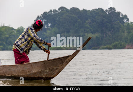 Nakasong, Laos - Aprile 22, 2018: Senior donna barca a remi in legno longboat attraverso il fiume Mekong da Nakasong a Don Det isola vicino a bord cambogiano Foto Stock
