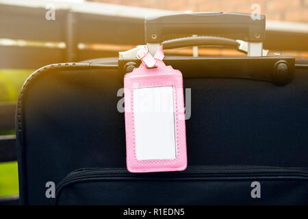 Femminile rosa bagagli vuoti targhetta fissata al bagaglio nero valigia. Perso, trovato elemento di design concept. Foto Stock