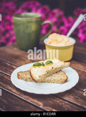 Giallo delizioso uovo e maionese sulla pasta di pane integrale, prima colazione snack ricetta, fiori di colore rosa sullo sfondo, base in legno. Foto Stock