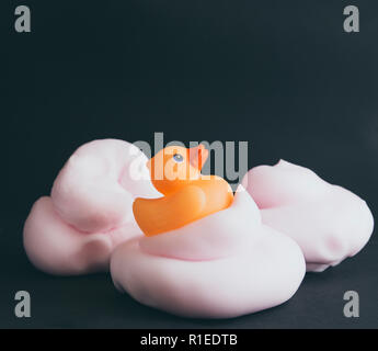 Arancione bagno gomma anatra sul mucchio di gommapiuma rosa isolato su sfondo nero. Foto Stock