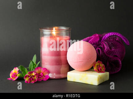 Wellness spa therapy coccole prodotti su sfondo nero, rosa candela bruciando, caldo dell'umore. Bagno rosa bomba, fatto a mano sapone, spugna rosa, rosa la masterizzazione Foto Stock