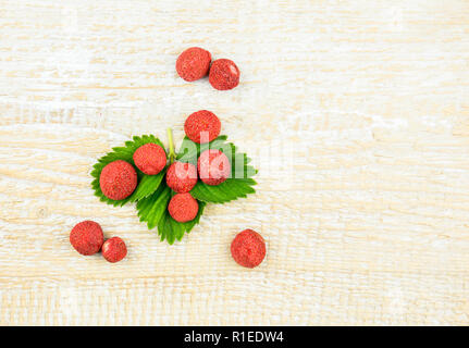 Liofilizzato intere e pezzi di fragole su verde foglia di fragola snack sano e pieno di vitamine e nutrizione su legno naturale dello sfondo. Foto Stock