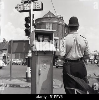 1967, storico, un poliziotto britannico si trova in corrispondenza di un incrocio a Aylesbury High Street, Bucks, Inghilterra dal monitor del traffico, il 'Electro-Matic' di traffico del sistema di controllo. Il gruppo elettro-meccanico di tecnologia fu usata con i semafori per regolare il flusso del traffico. Foto Stock